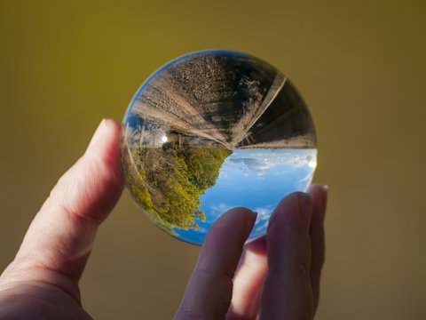 Woman hand holding glass ball with panoramic view of countryside and sky/ Concept for environment