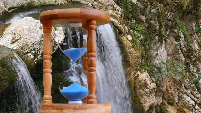 Hourglass on the background of a mountain stream