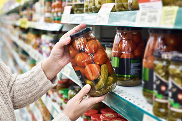 Hands with can of salted tomatoes and cucumbers in store