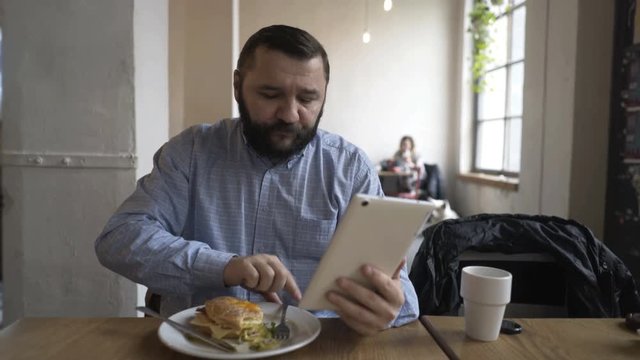 Young man with tablet computer eating lunch in cafe 
