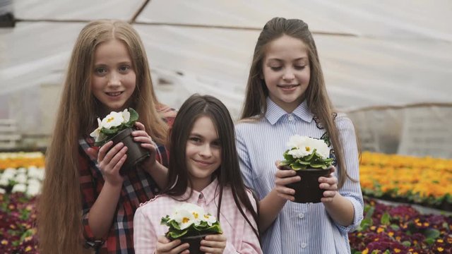 Three girls stretching flower pots to camera with smile