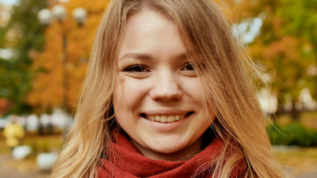 Face of young attractive girl close-up. Smiling girl posing on camera among colorful autumn park trees.