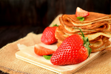 Fresh strawberries and golden crepes on a wooden board