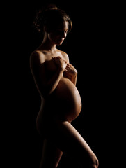 Silhouette of pregnant woman holds hands on belly on black background. Pregnancy, maternity, preparation and expectation concept