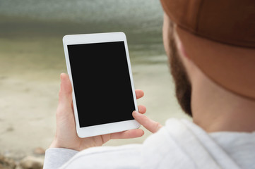 Close-up of a horde in a brown cap in the open air holds a white tablet pc in his hands. A bearded man looks at the tablet. OTS view from behind the shoulder. Makes a swap move with his finger