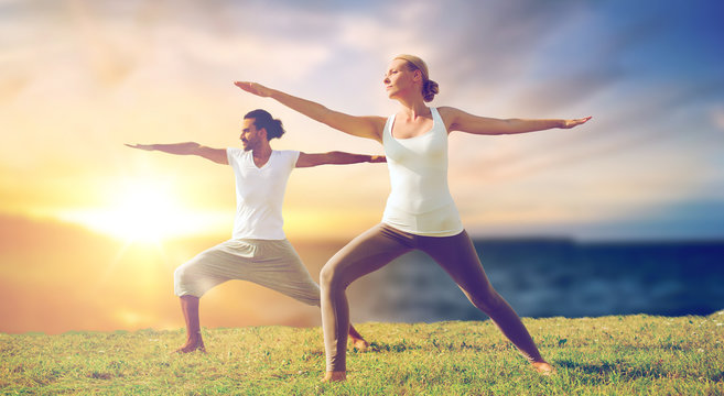 fitness and people concept - couple making yoga warrior pose outdoors over sea background - Powered by Adobe