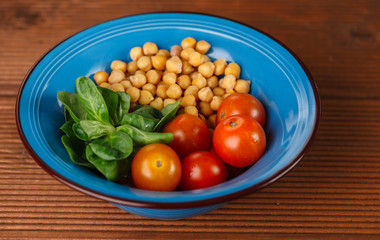 Healthy lunch in blue bowl: chickpeas, cherry tomatoes, corn salad. Top view