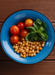 Healthy lunch in blue bowl: chickpeas, cherry tomatoes, corn salad. Top view