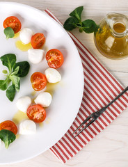 classic Italian Caprese salad with tomato cherry, salad corn on white plate. Textile decorated