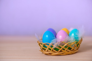 multicolored painted Easter eggs lie in basket with feathers, copy space
