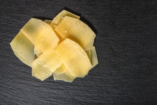 top down of tasty fresh yellow thin slice parm cheese on black stone slate background, close up