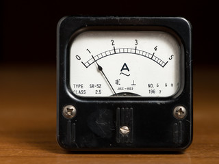 An old black analog ampere meter on a wooden table