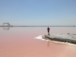 Salzig - Ein Mann schaut auf einen rosa Salzsee. Er steht auf einem Steinvorsprung und schaut in...