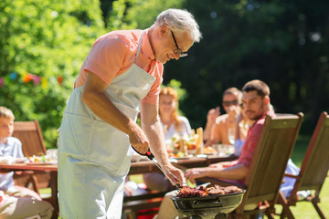 food, people and family time concept - senior man cooking meat on barbecue grill at summer garden...