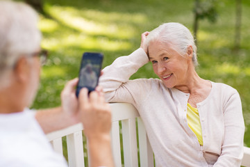 technology, retirement and old people concept - happy smiling senior couple with smartphone photographing in summer park