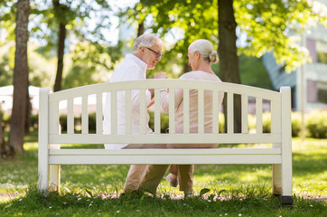 old age, relationship and people concept - happy senior couple sitting on bench at summer park - Powered by Adobe
