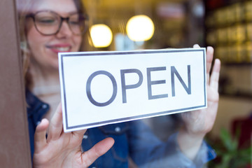 Beautiful young woman hanging the open sign in the store.