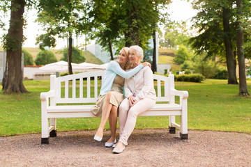 family, generation and people concept - happy smiling young daughter with senior mother sitting on park bench and hugging