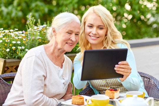 Family, Technology And People Concept - Happy Smiling Young Daughter With Tablet Pc Computer And Senior Mother At Cafe Or Restaurant Terrace