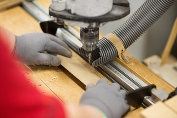 production, manufacture and woodworking industry concept - hands of carpenter working with drill press and board at workshop