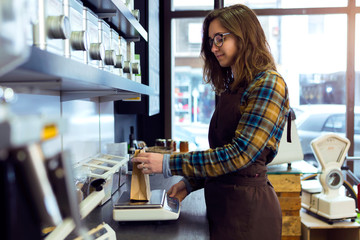 Beautiful young saleswoman weighing coffee beans in a retail store selling coffee.