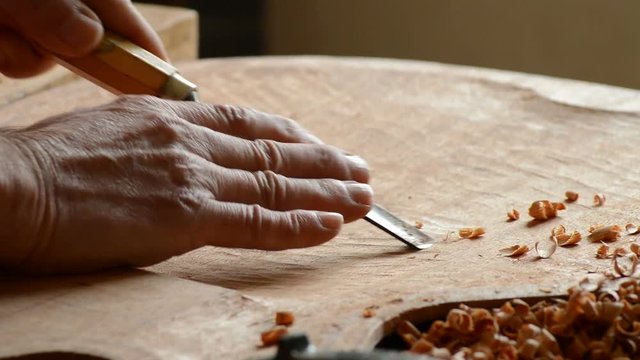 Luthier carving the bottom of a guitar cover with a gouge in the workshop