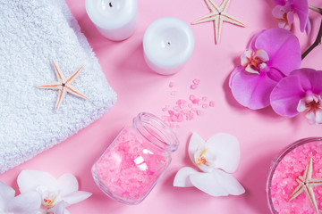 Spa background, flat lay layout with pink sea salt, candles and aroma oils and cosmetic care products on a pink background