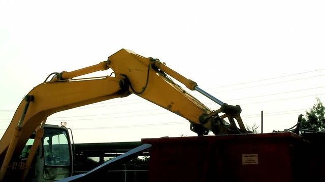 An excavator is loading scrap metal junk into a bin at a garbage dump or recycling center. Waste includes household appliances and roofing iron. Part 2 (joins part 1 with a 2 second overlap.)