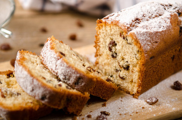 A homemade cake with raisins and powdered sugar is cut on wooden table. White napkin