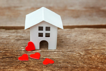 Obraz na płótnie Canvas Miniature white toy house with red hearts on a rustic old vintage wooden background. Mortgage property insurance dream home concept
