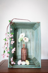 Easter eggs and spring flowers, gerbera or daisy, in a vintage pink vase inside an old wooden fruit crate