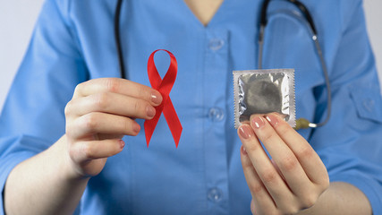 Doctor holding red ribbon condom, sexually transmitted diseases warning, AIDS