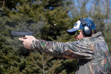Fototapeta premium Man shooting a pistol; ejected cartridge case in the air.