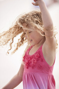 Young girl with curly blonde hair twirls around as she dances while posing for a portrait.