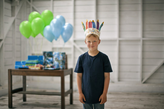 Portrait of a young boy standing in front of a table of presents and balloons.
