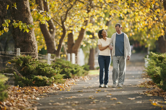 Female nurse helping an elderly man to walk through a park.
