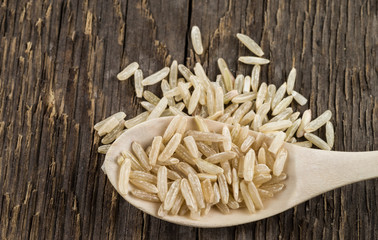 One of the varieties of rice on a wooden spoon against a background of rough wood texture.
