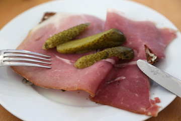 schinkenbrot mit gewürzgurke auf einem weißen teller und messer und gabel