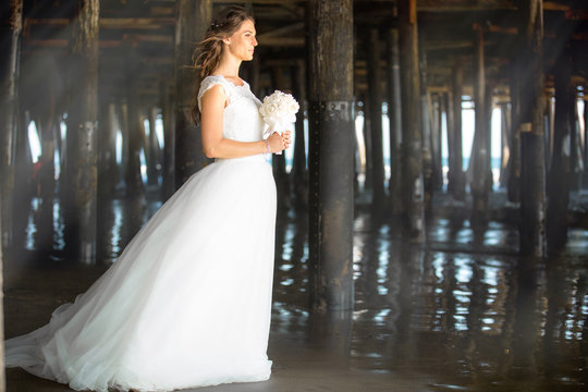 Bride in white dress standing elegant, classic, traditional, glamorous, next to pier pillars