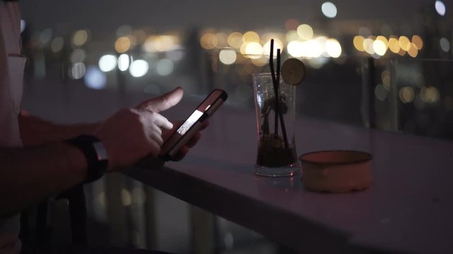 Man standing on the roof at night and browsing photos on smartphone
