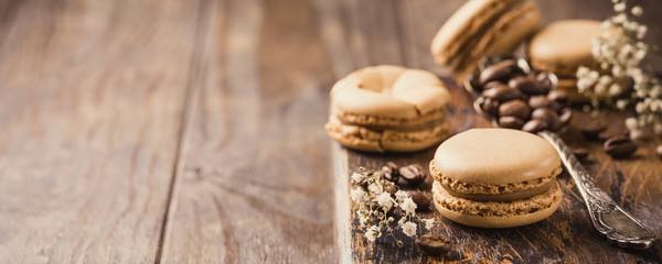 French coffee macarons with ganache filling with coffee beans on old wooden board on rvintage background. Holidays food concept with copy space. Banner.