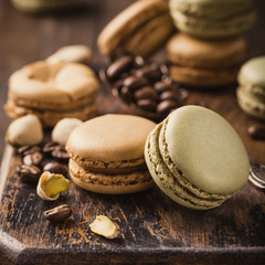 French coffee and pistachio macarons with ganache filling with coffee beans on old wooden board on rvintage background. Holidays food concept.