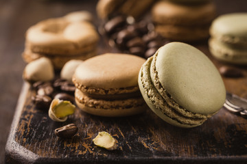 French coffee and pistachio macaroons with ganache filling with coffee beans on old wooden board on rvintage background. Holidays food concept.