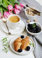 Morning breakfast with cup of coffee, croissants, fresh berries and pink flowers tulips on white tray, brown sugar