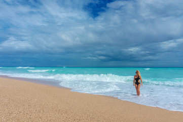 beautiful blonde girl in a black swimwear  walking on an empty Caribbean beach