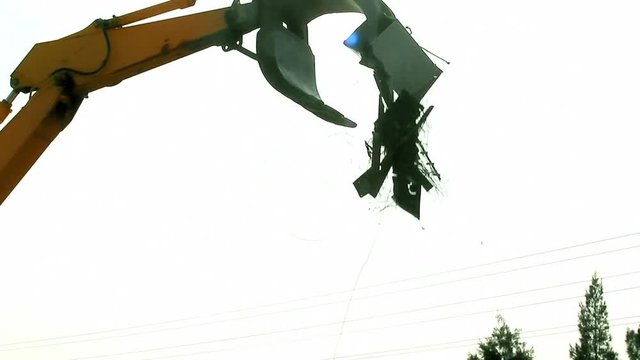 An excavator is loading scrap metal junk at a garbage dump or recycling center. The waste includes appliances and roofing. A microwave is stuck on the claw. Part 1 (joins part 2 with a 2 sec overlap.)