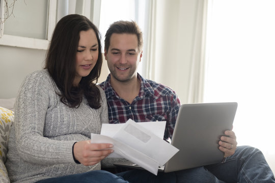 Mid adult couple sitting on sofa and looking at letter, man holding laptop