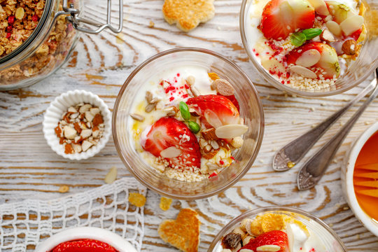 Natural yogurt with fresh strawberries, granola, honey, nuts and seeds in a glass dishes, top view. Delicious breakfast or dessert. Healthy eating concept. 
