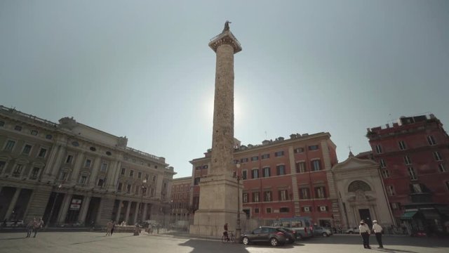 The morning sun shines brightly behind the Column of Marcus Aurelius in the Piazza Colonna in Rome