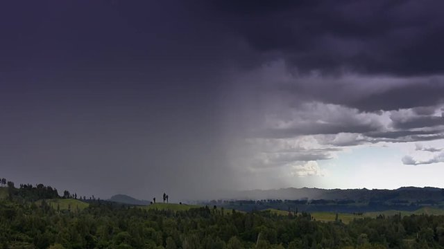 Dark storm clouds approach over a rural landscape of farms and woods, bringing rain. Time lapse footage. 